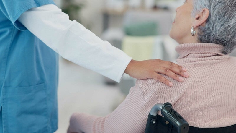 Hospital Volunteer comforting an elderly female patient who is in a wheelchair