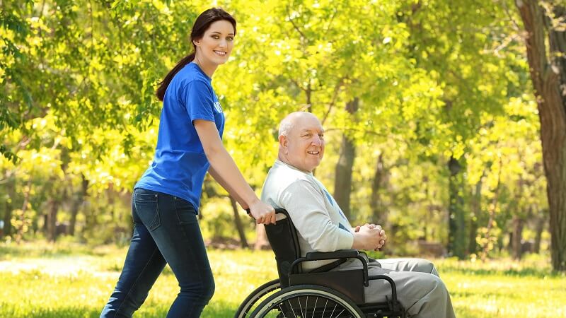 Hospital Volunteer pushing a patient who is in a wheelchair outside on a nice summer day