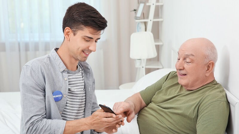 Hospital Volunteer helping an older male patient use their smartphone