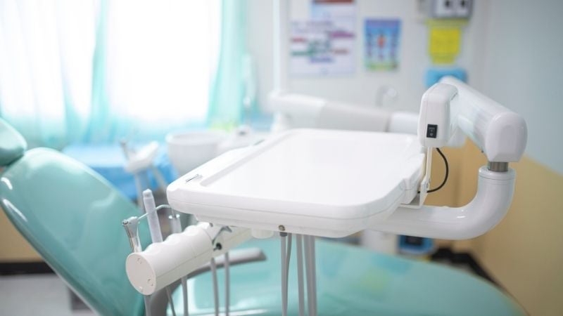 A dentist's office contains a teal chair and an instrument table