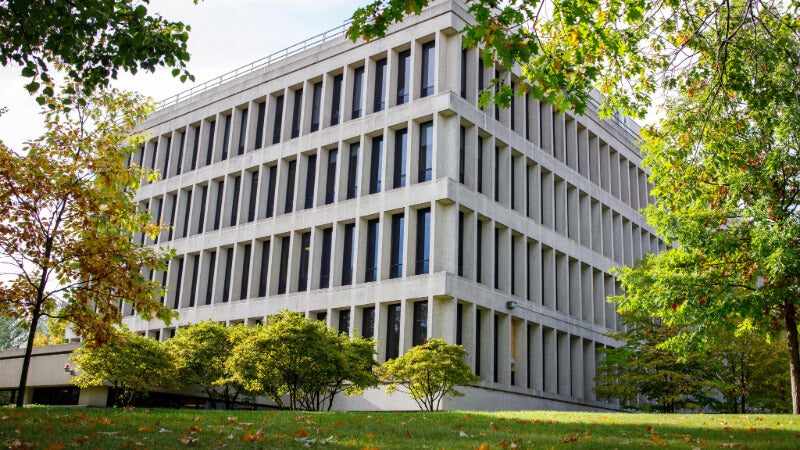 A hospital building is shown. It is grey and has many long windows. 