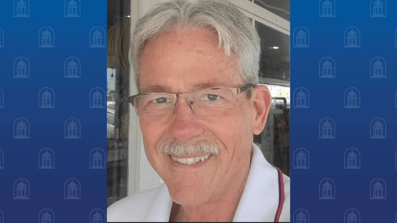 An elderly man with glasses and a mustache smiles for the camera.