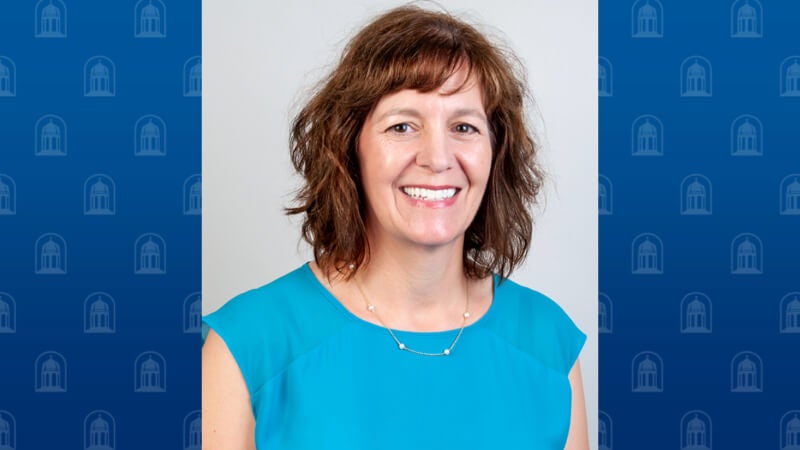 A woman with shoulder-length hair is smiling. She is wearing professional attire.