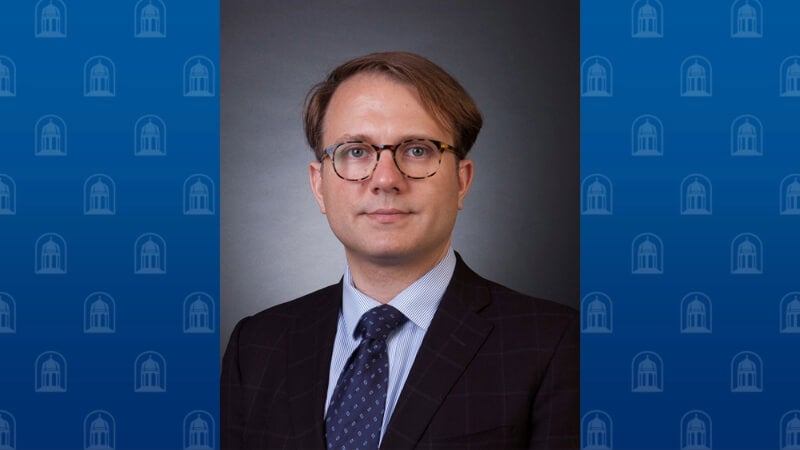 A man with glasses is photographed wearing a suit and tie. 