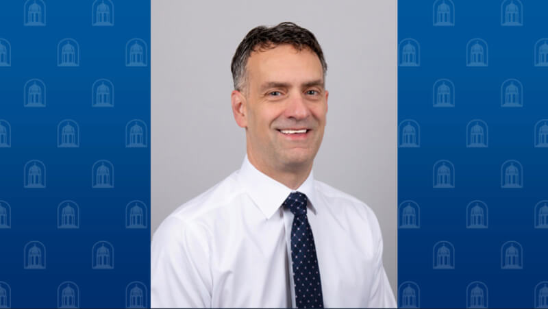 A man wearing a white button down shirt and tie smiles for the camera 