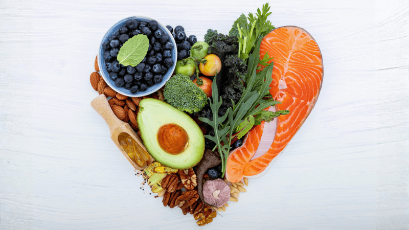 Heart healthy foods like salmon, blueberries, and avocado are arranged into the heart shape.