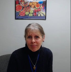 A woman, Lisa Roman, is photographed sitting in front of a photo of fresh fruits. 