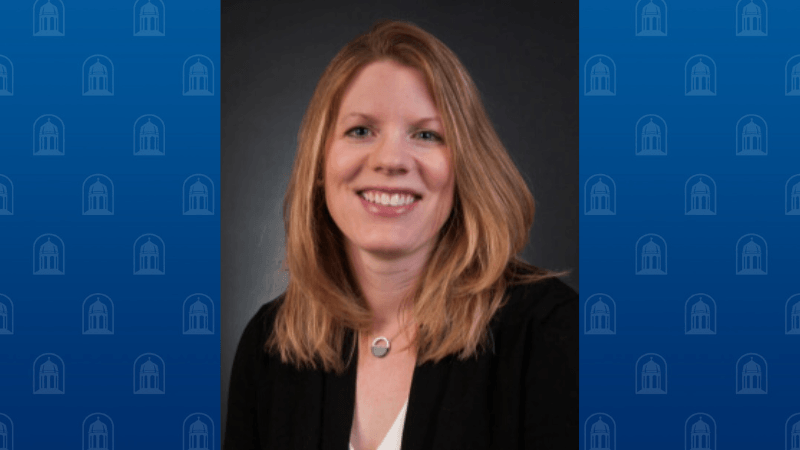 A woman with shoulder length blonde hair is photographed. She is smiling and wearing professional attire. 