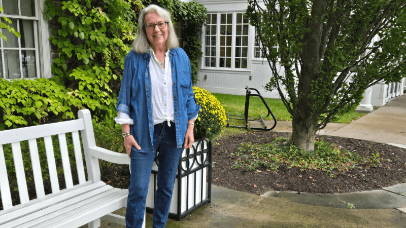 A woman, Georgia Meeter, is photographed outside Bassett Medical Center in Cooperstown. She is wearing jeans, a white button down shirt, and a denim overshirt. 