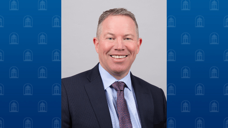 A man, Dr. Maximillian Lincoln, is photographed. He is wearing a suit and tie and he is smiling. 