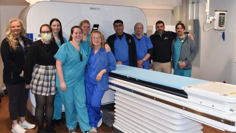 Ten healthcare workers are photographed standing around a CT scanner