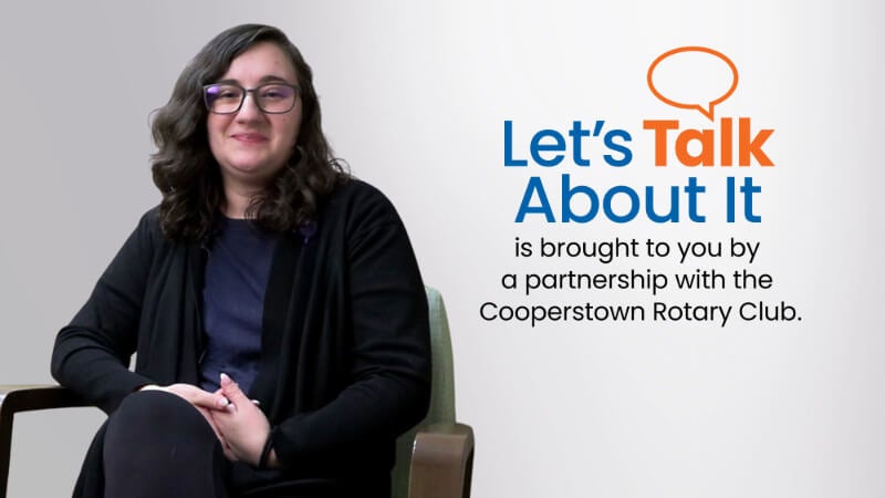 A woman is photographed sitting in a chair. Text beside her reads 'Let's Talk About It is brought to you by a partnership with the Cooperstown Rotary Club" 