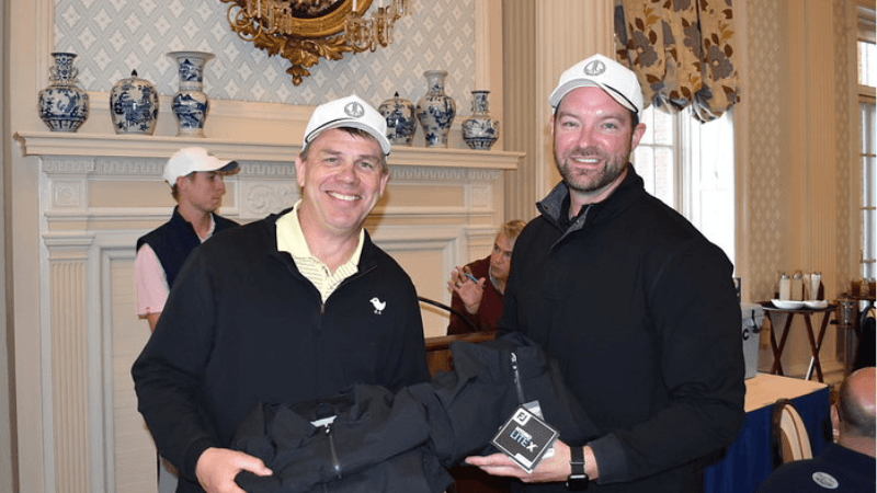 Two golfers stand together for a photo. They are each holding a gift.