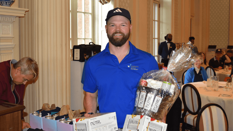A golfer stands for a photo. He is holding a gift.