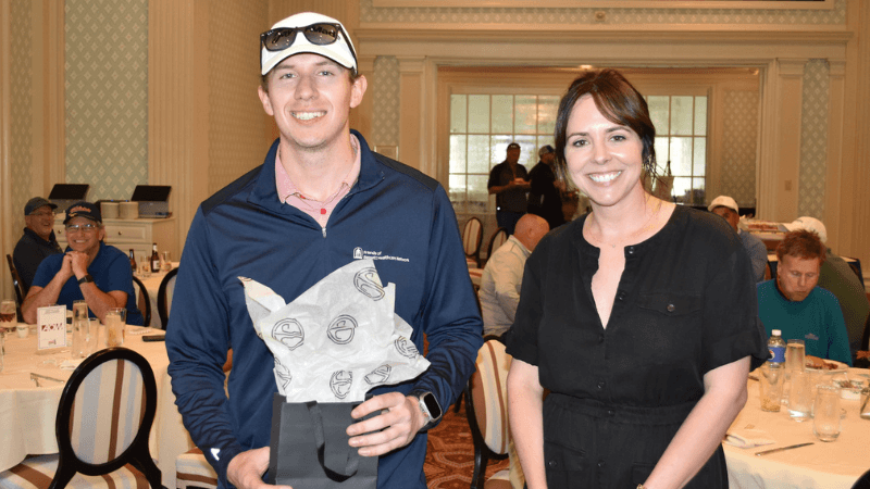 Two golfers stand together for a photo. One of them is holding a gift.