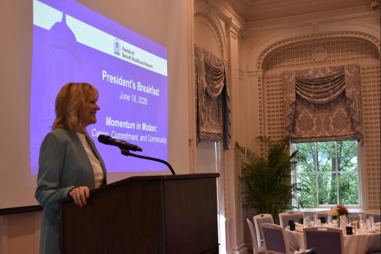  A person stands at a podium. A presentation side is projected on a screen behind them.