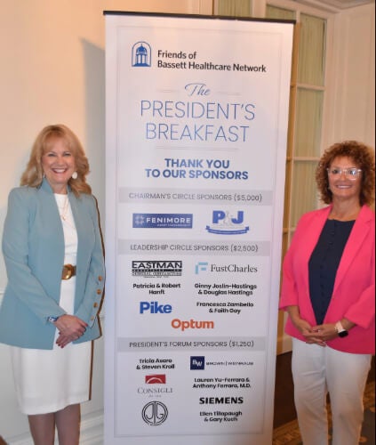 Two people stand next to a banner that includes the logos for the breakfast's sponsors