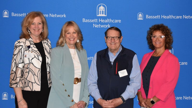 Four people stand side by side in front of a Bassett Healthcare Network backdrop. They are all smiling for the camera. 