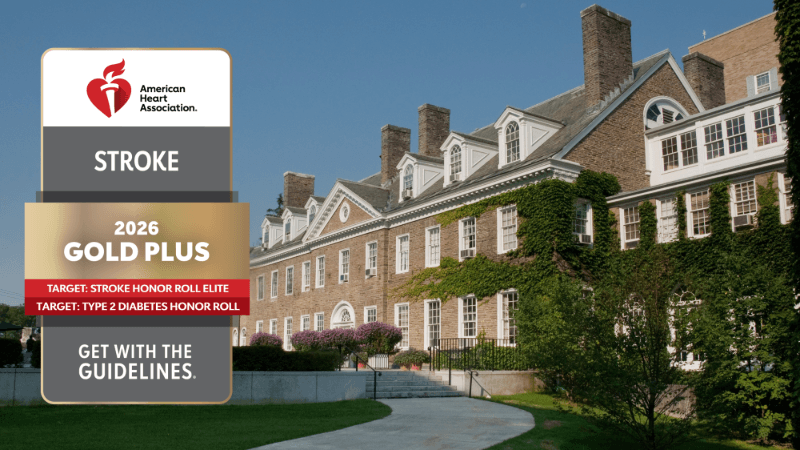 A photo of Bassett Medical Center has a seal edited into it. The seal reads "American Heart Association Stroke 2026 Gold Plus, Target: Stroke Honor Roll Elite, Target: Type 2 Diabetes Honor Roll, Get with the Guidelines"