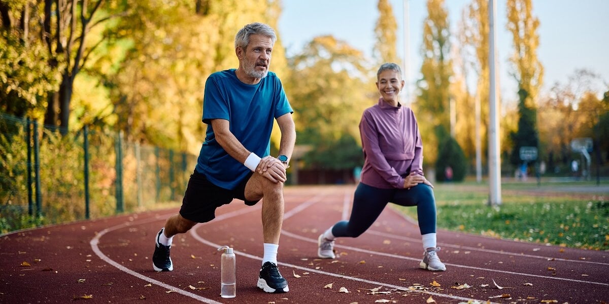 An older man and woman stretching, getting ready to run on a track for cardiovascular exercise
