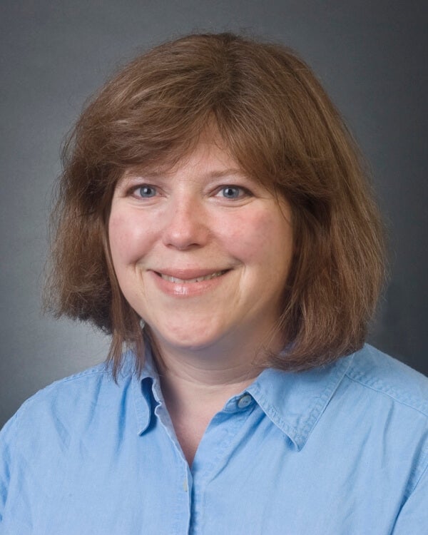 A woman is photographed from the shoulders up. She is wearing professional attire.