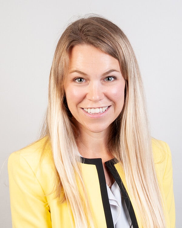 A woman is photographed from the shoulders up. She is wearing professional attire.