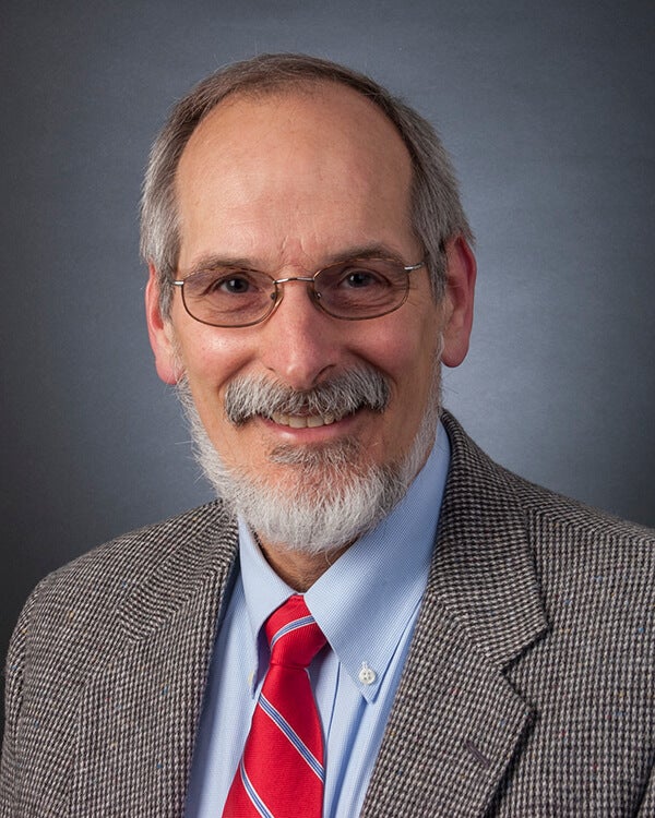 A man is photographed from the shoulders up. He is wearing professional attire.