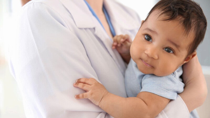A person wearing a white doctor's coat holds an infant in their arms.