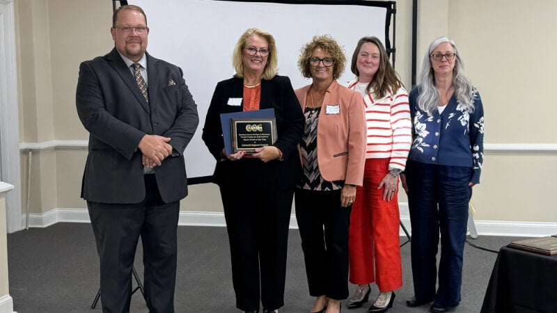 A group of five people stand for a photo. One of them is holding a plaque. 