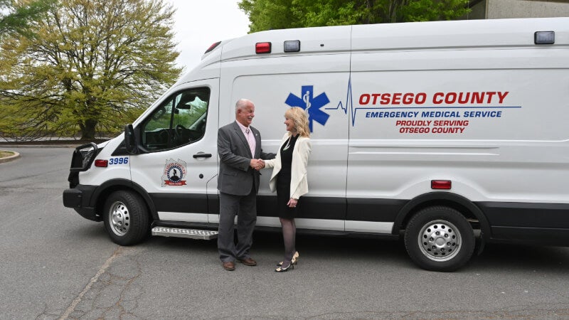 Ed Frazier and Staci Thompson shake hands in front of an emergency transport vehicle.