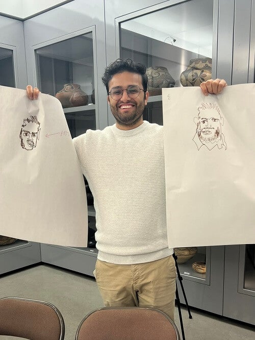 Sagar Ghimire, PGY3 IM Resident holds up two portraits drawn during an observational workshop at Fenimore Art Museum.