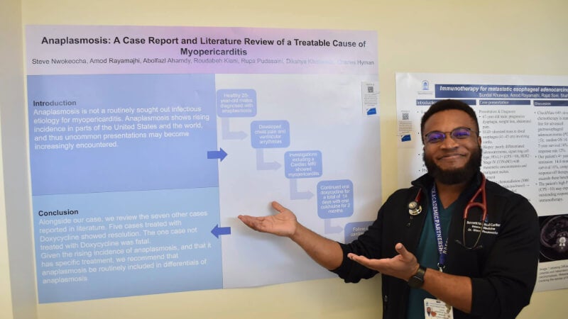 A man gestures towards a poster showcasing his research on anaplasmosis.