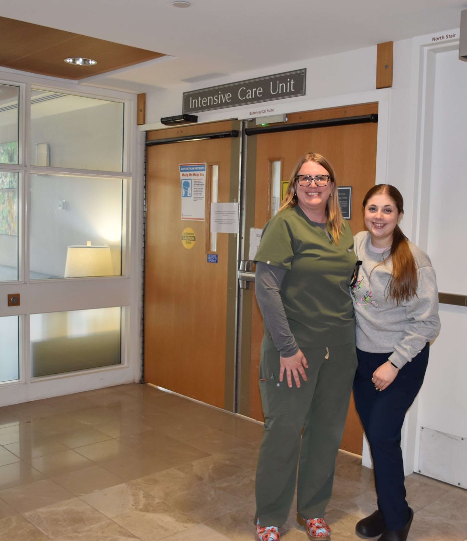 Two women stand togehter inside a hospital outside a door that says Intensive Care Unit.