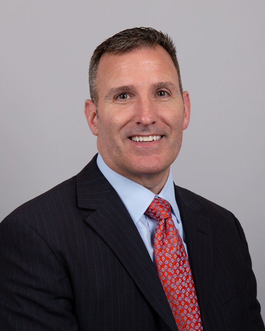 A man, Michael Guiry, is photographed. He is wearing professional attire and smiling for the camera. 