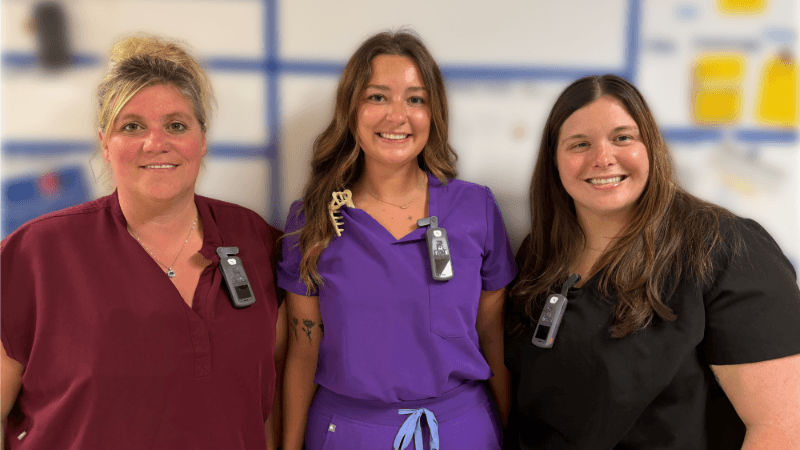 Three caregivers wearing scrubs are photographed. They are wearing Vocera Smartbadge devices.