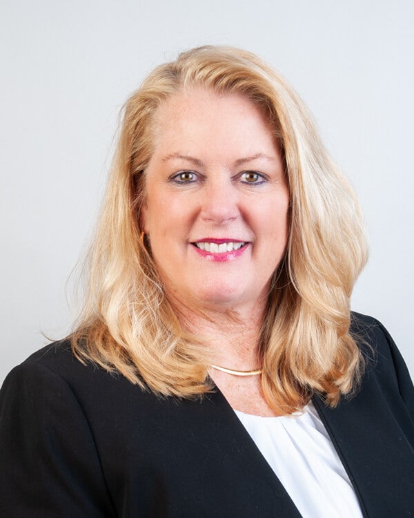 A woman, Susan Oakes Ferrucci, is smiling for the camera. She is wearing professional attire.