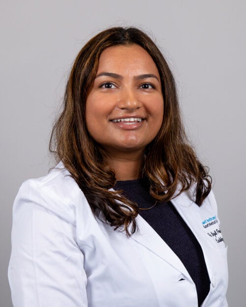 Dr. Anjail Prakash is photographed wearing a white coat and black outfit.