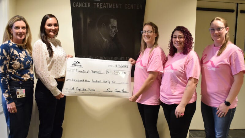 Five women stand with a ceremonial check. Three of them are wearing pink Breast Cancer Awareness t-shirts.