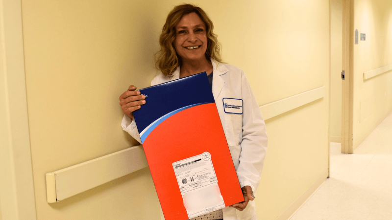 A woman in a white doctor's coat is photographed holding a box that appears to contain a medical device.