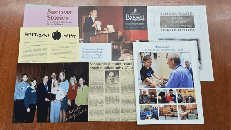 A series of documents and photos are photographed. They show some of the history of the School-Based Health Program.