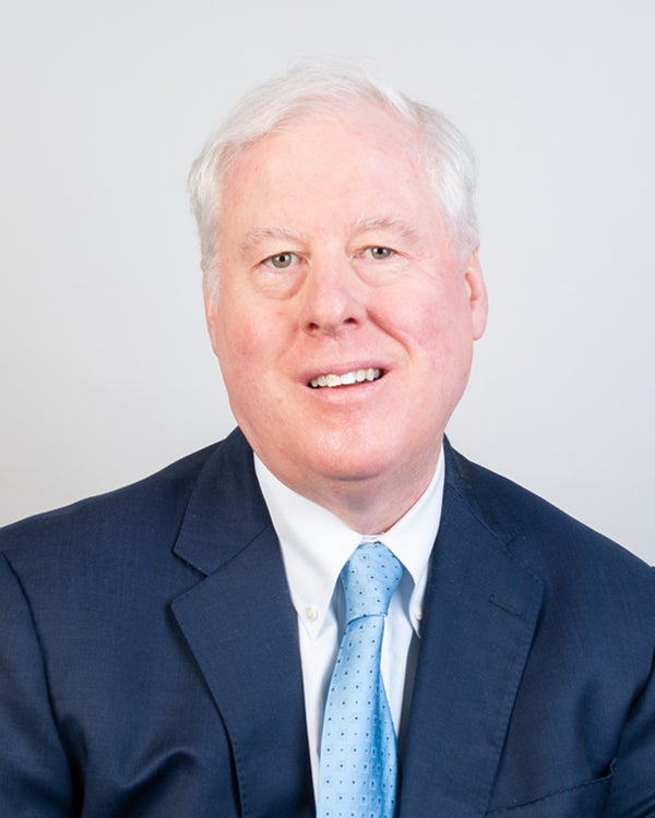 A man with white hair, wearing a suit, smiles for the camera.