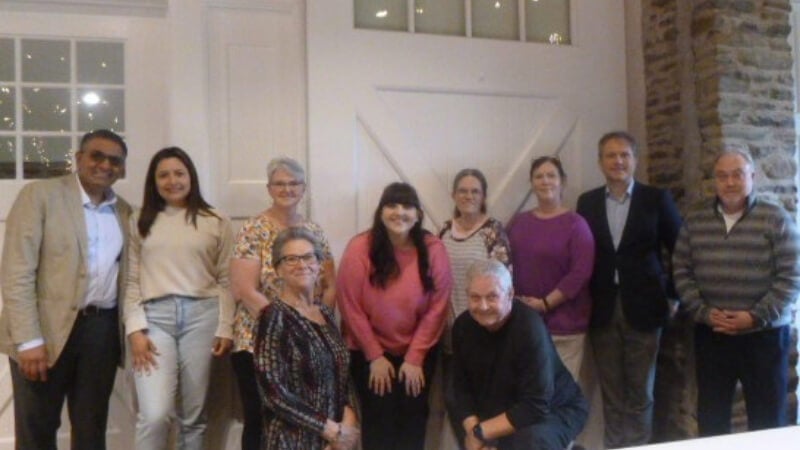 10 people stand in a group for a photo. They appear to be in a barn-like venue.