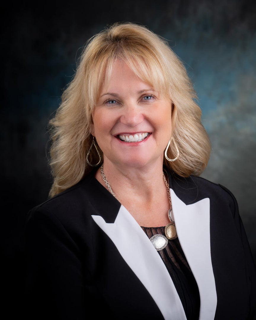 A woman, Staci Thompson, is photographed. She is wearing professional attire and smiling for the camera. 