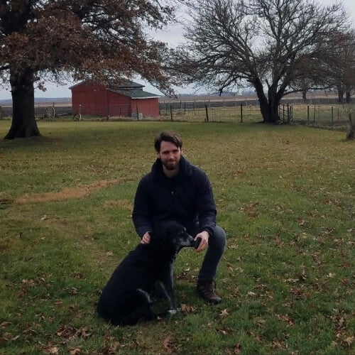A man, Dr. Malone, is photographed with a dog in front of a red barn.