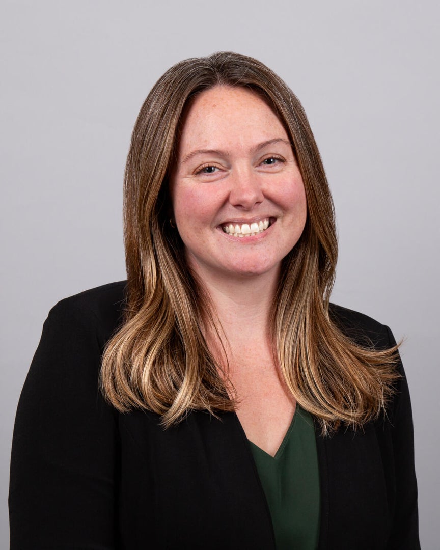 A woman, Erin Vollmer, is wearing professional attire is smiling for the camera. 